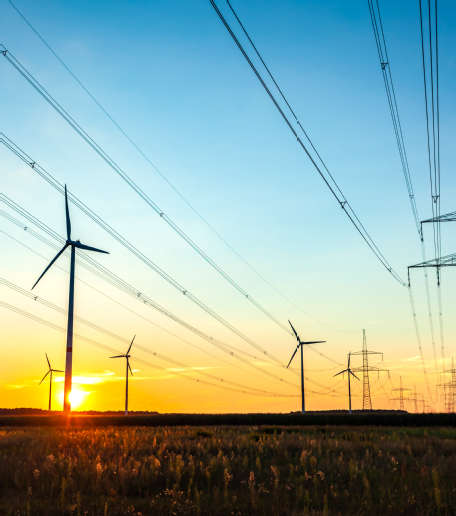 Hochspannungsleitungen mit Windkraftanlagen im Hintergrund bei Sonnenuntergang